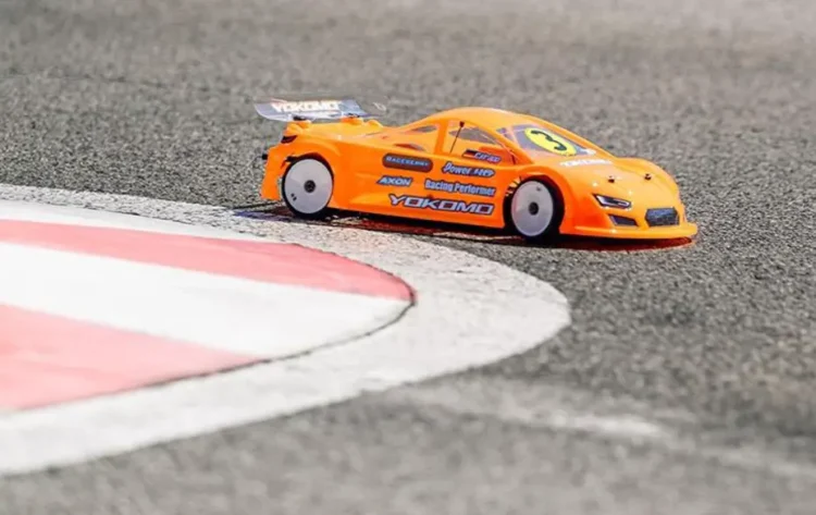 An RC touring car leaning heavily on a high-grip carpet track corner